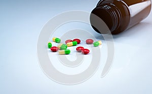 Green and yellow capsules with red tablets pills near brown drug bottle on white background. Pharmaceutical industry. Painkiller