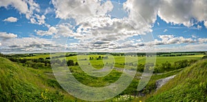 Green, yellow field forest and clouds on blue sky in summer, sunny day.