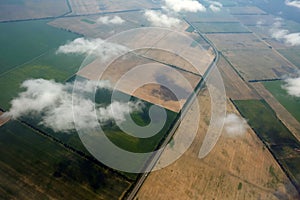 Green and yellow fields and clouds top view from an airplane.