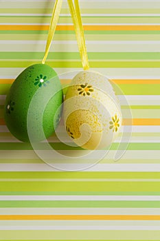 Green and yellow hanged Easter eggs on striped background