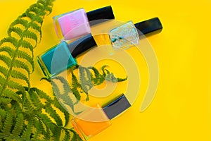 Green and yellow, pink, shiny nail Polish lie on a yellow background
