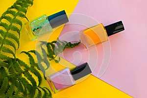 Green and yellow, pink, shiny nail Polish lie on a yellow background