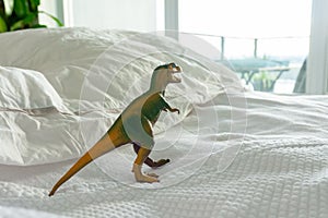 Green and yellow plastic dinosaur toy on parent`s bed depicting a family home where kids live