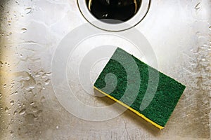 Green and yellow scrubing sponge lying in scratch and wet sink with garage disposal