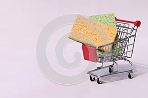 Green and yellow sponge in a metal basket on a white background. Space for text. The concept of buying cleaning products