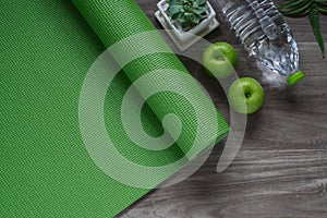 Green yoga mat on a wooden background with green apples and bottle of water. Active healthy lifestyle background concept.