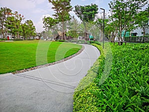 Greenery bush and trees in garden with gray curve pattern walkway, sand washed finishing on concrete paving and brown gravel