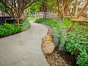 Greenery bush and trees in garden with gray curve pattern walkway, sand washed finishing on concrete paving and brown gravel