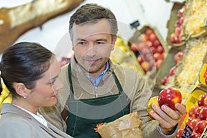 Greengrocer serving apple to customer