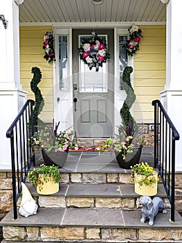 Greenish front door of the house, decorated with a wreath, flowers and figurines. Facade of a house with a porch and columns