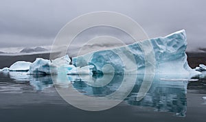 Greenland, blue iceberg with perfect reflection in the fjord with dramatic mood of the sky