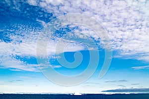 Greenlandic blue sky with altocumulus clouds over dark blue Arctic Ocean with iceberg, Greenland