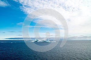 Greenlandic landscape with altocumulus clouds on blue sky over dark blue Arctic Ocean with iceberg, Greenland