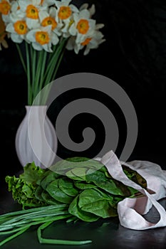 Greens for cooking, spinach, parsley, onions, dill on a background of blooming daffodils.