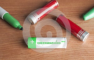 Greenwashing concept: some batteries and a green marker on a wooden table. Greenwashing is a communication technique aimed at