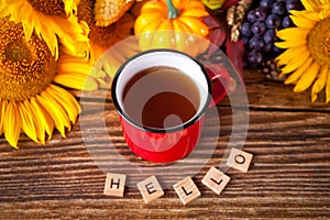 Greeting autumn card. Composition with pumpkin, autumn leaves, sunflower, red mug of tea and wooden text Hello on the wooden