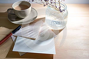 Greeting card and envelope from natural recycling paper, pen, coffee cup and a glass vase with sunlight reflections in the morning