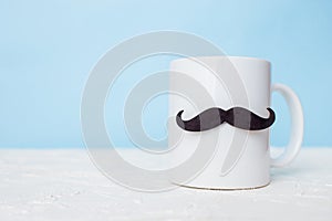 Greeting card fathers day holiday concept. White cup with mustache on blue pastel background