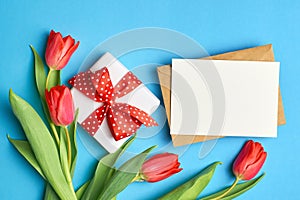 Greeting card mockup with gift box, envelope and red tulips on blue paper background