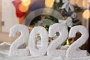 a greeting card with a happy new year 2022 on the background of a fireplace, a Christmas tree, with bright lights of a