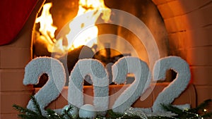a greeting card with a happy new year 2022 on the background of a fireplace, a Christmas tree, with bright lights of a