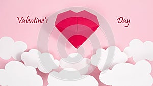 Greeting card. Happy Valentine`s Day. A red voluminous origami heart floats above slowly moving white clouds. Pale pink background