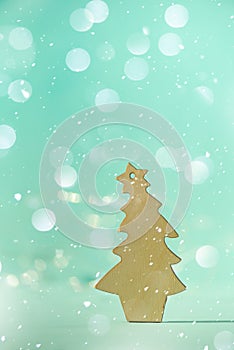 Greeting card in minimal style. Wooden Christmas tree on blue background with copy space, lights bokeh, snow. New Year party.