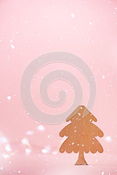 Greeting card in minimal style. Wooden Christmas tree on pink background with copy space, lights bokeh, snow. New Year party.