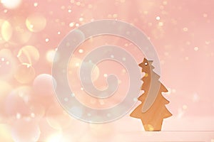 Greeting card in minimal style. Wooden Christmas tree on pink background with copy space, lights bokeh, snow. New Year party.