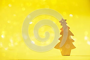 Greeting card in minimal style. Wooden Christmas tree on yellow background with copy space, lights bokeh, snow. New Year party.