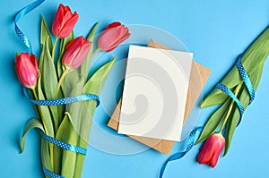 Greeting card mockup with envelope and red tulips flowers with ribbon on blue paper background