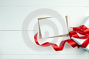 Greeting card mockup with paper envelope and red ribbon and gift box on white table