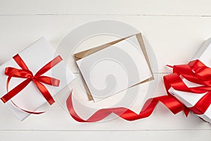 Greeting card mockup with paper envelope and red ribbon and gift box on white table