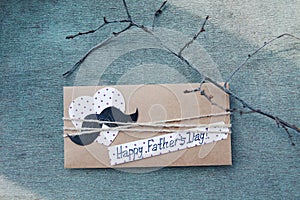 Greeting card with paper heart, mustache, text Happy Father`s day, branche on blue wooden background. Concept International Fathe