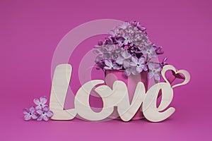 Greeting Card with spring lilac flowers and word Love on pink background, copy space. Concept of Valentine Day
