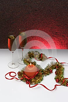 Greeting card template made of golden and green tinsel with red christmas balls, red ribbon, orange candle and two glasses of cham