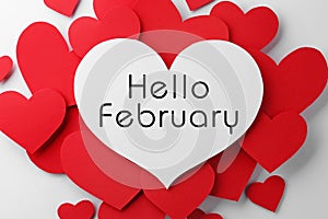 Greeting card with text Hello February. Many red paper hearts and one with text on white background, flat lay