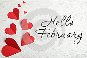 Greeting card with text Hello February. Red paper hearts on white wooden background, flat lay