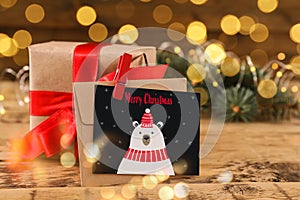 Greeting card with text Merry Christmas and gift on wooden table