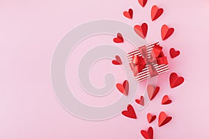 Greeting card for Valentine day with gift box and paper red hearts on pink table top view. Flat lay