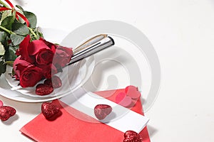 Greeting card for Valentine`s Day or Women`s Day. Red roses with ribbon on a white plate of the gala table and a love letter wit