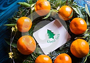 Greeting card with wish `Good luck` surrounded with fresh mandarins and spruce branches with garland lights