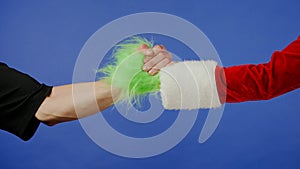 Greeting gestures of man and Grinchs hairy green hand on isolated blue background. Gift kidnapper cosplay