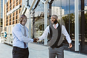 Greeting and handshake of two afro american businessmen partner against the backdrop of a modern building exterior