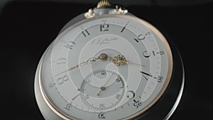 Grey antique pocket watch on a stand rotating on a black isolated background. Round silver retro clock with a white dial