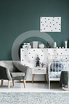 Grey armchair, bedside table, metal bed and dotted wall decorations in a dark green bedroom interior