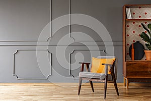 Grey armchair with orange pillow standing in real photo of dark