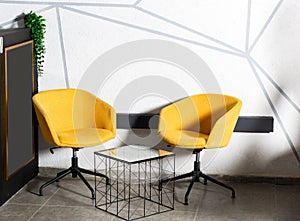 Grey armchair with pillows on studio yellow background.