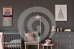 Grey armchair with pink pillow between bed and cabinet in child`