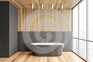 Grey bathtub on wooden floor in bathroom near window, wooden design